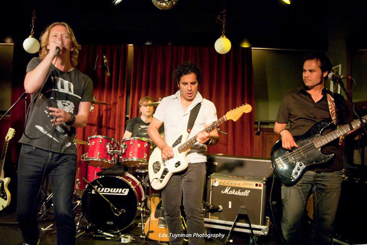 Een band speelt live op het podium van de Taverne voor het rode gordijn